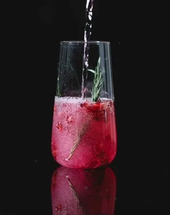 Red cocktail with ice and mint sprig in highball glass